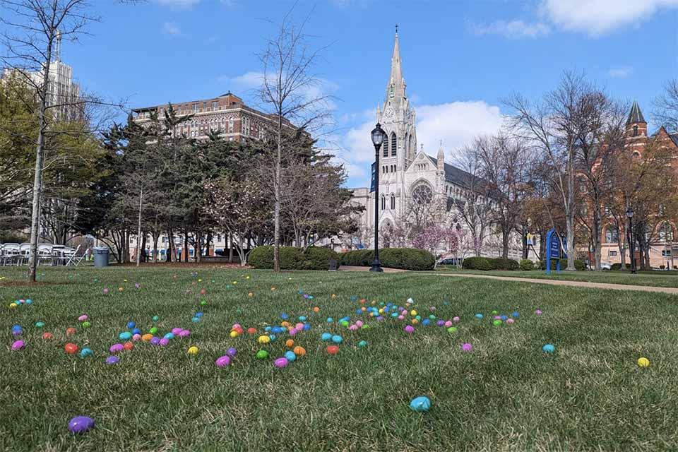 Colorful easter eggs spread out on a green lawn with College Church and Dubourg Hall in the background on a sunny day