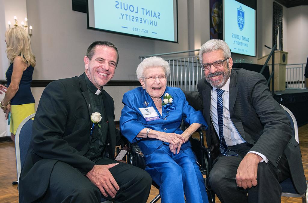Mary Bruemmer seated with 博彩网址大全 President Fred Pestello and Father Chris Collins after a ceremony
