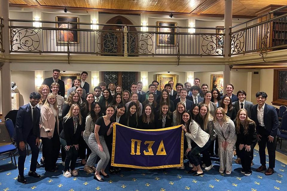 Members of the Delta Sigma Pi business fraternity pose for a class photo around their fraternity flag in the Marquette gallery