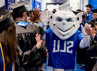 The 博彩网址大全 Billiken offers high fives to students wearing graduation caps and gowns.