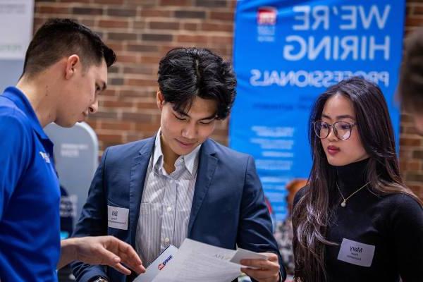 Two students with 博彩网址大全 Business School rep having a conversation about paperwork