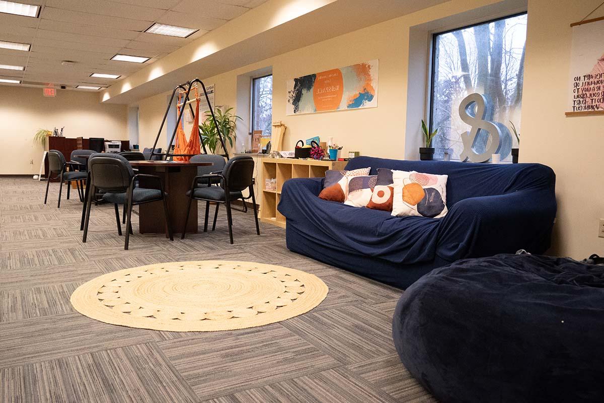 想象一个铺着地毯的房间, a round area rug, a comfy looking couch, bean bag chair, 桌子和椅子.