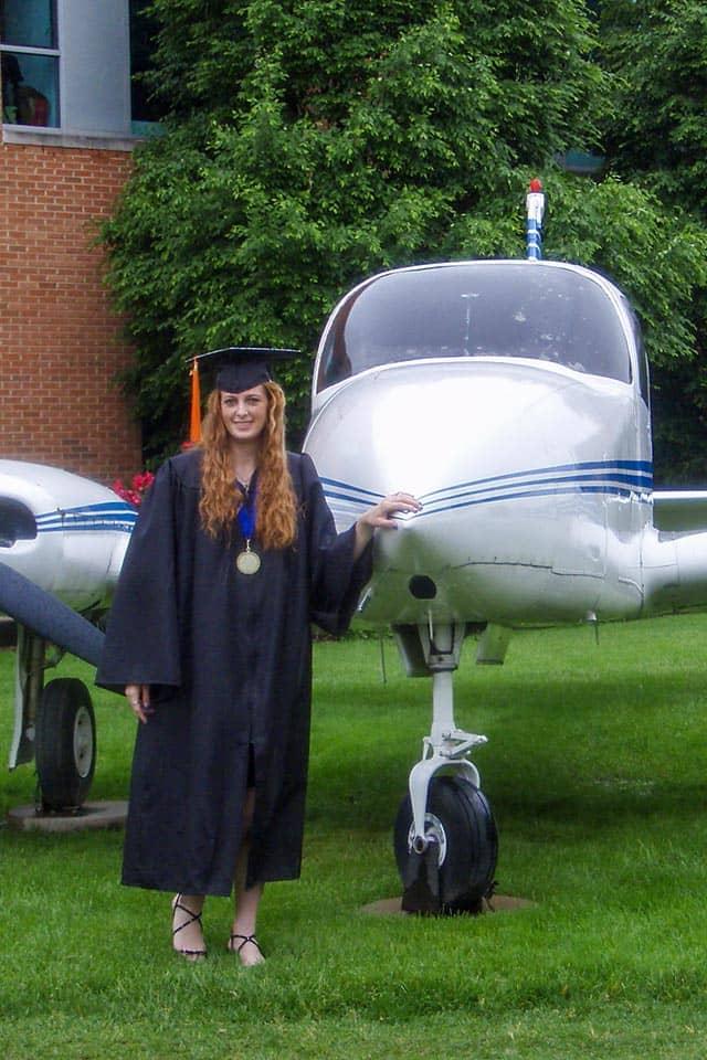 Sullivan stands near the plane in front of Parks Hall in her graduation robe.
